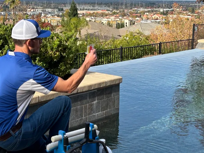 Pool technician testing water chemistry at the edge of a residential pool